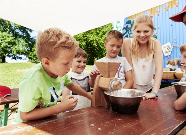 Drei Jungen* mahlen Mehl mit der Hand. Eine junge Frau* unterstützt sie. 