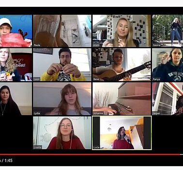 Screenshot einer Videokonferenz mit 14 Teilnehmenden. Einige halten ein Musikinstrument.