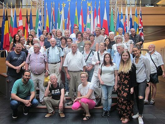 Eine Gruppe von älteren und jüngeren Menschen steht vor einem Wals aus Flaggen der Länder Europas.