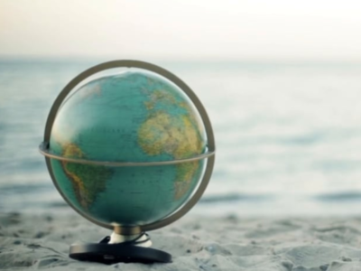 Ein Globus steht an einem Strand, das mehr im Hintergrund.