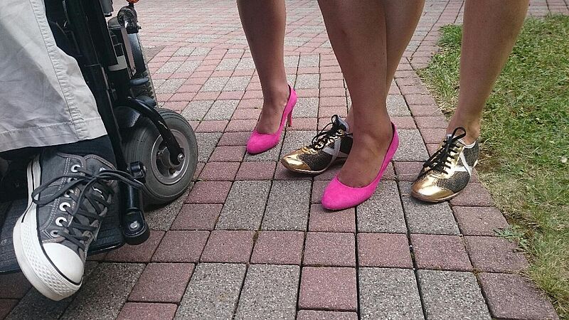 Drei Paar Füße in Turnschuhen, pinke Pumps und goldenen Halbschuhen.