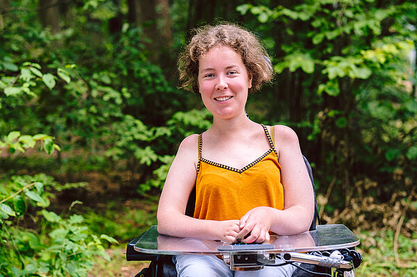 Sarah leistet ihr FSJ Kultur im Kulturamt Erlangen Sarah, die ihr FSJ Kultur im Kulturamt Erlangen macht, ist auf dem Bild zu sehen. Das Bild ist ein Porträt von Sarah. Sarah ist darauf angewiesen einen Rollstuhl zu benutzen. Auch das ist auf dem Bild sichtbar.